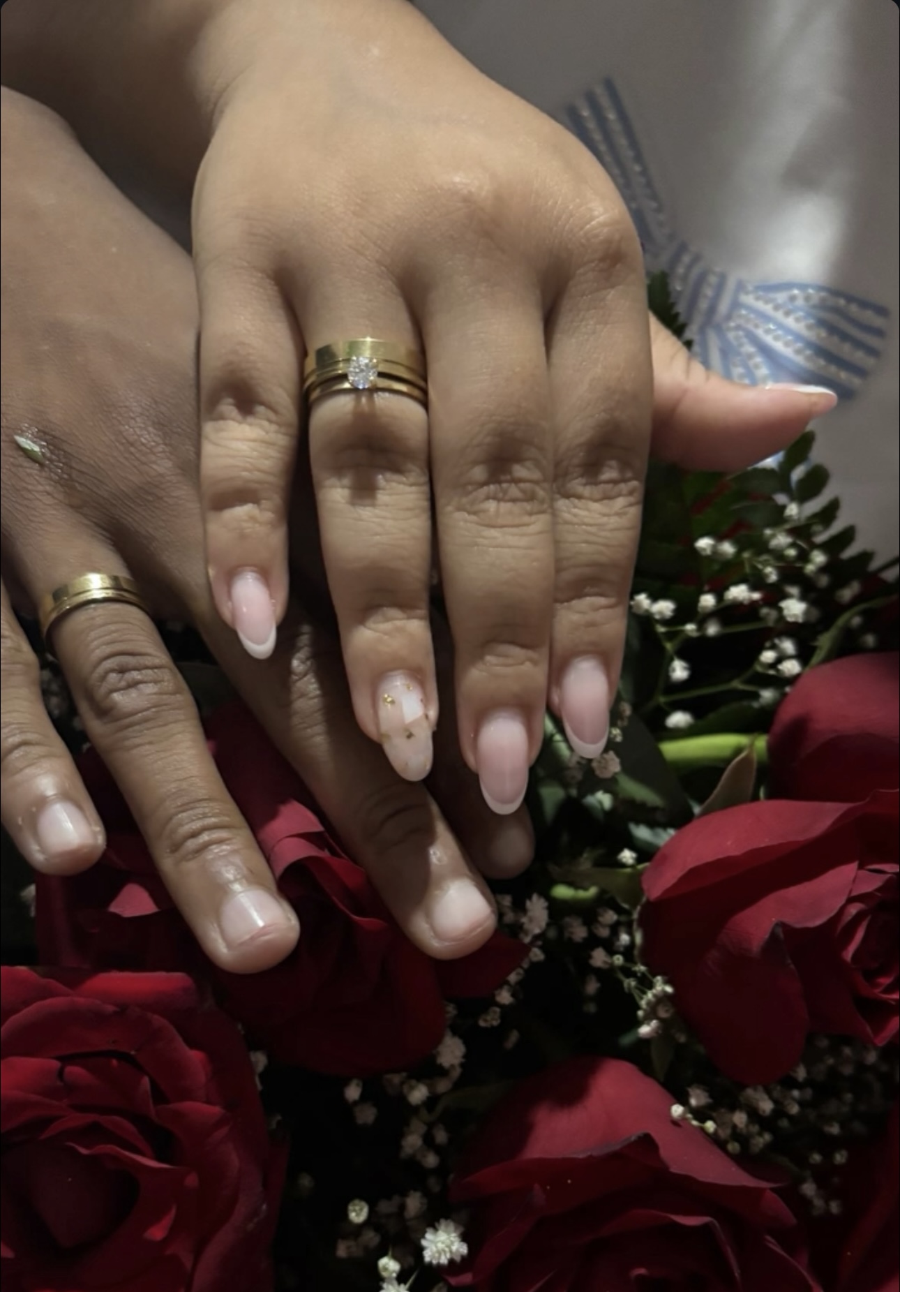 As mãos do casal com as alianças sobre um buquê de rosas